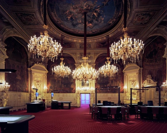 Ornate casino interior with crystal chandeliers, gaming tables, and detailed murals. Opulent architecture with a red carpet.