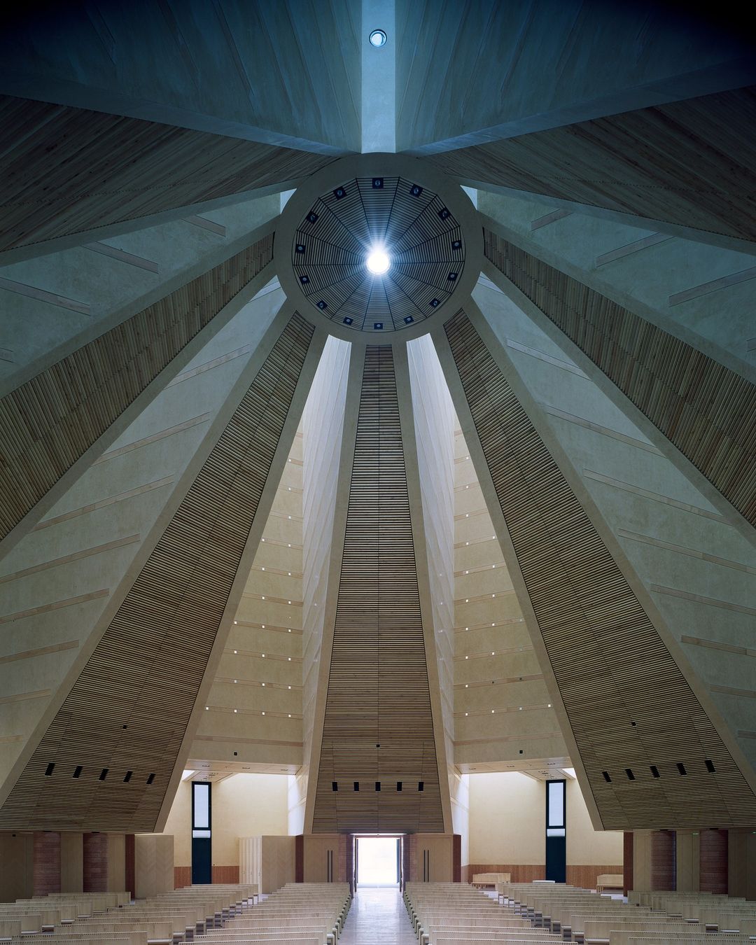 Interior view of a cathedral or church with geometric vaulted ceilings and rows of empty seating, showcasing modern architecture.