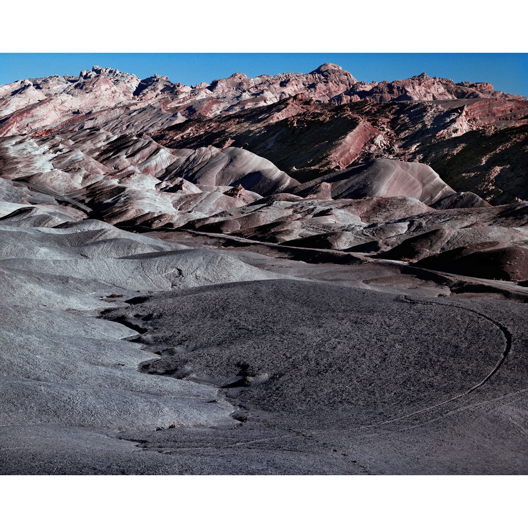 Panoramic vista of arid landscape with mountains and hills under clear blue sky, displaying varied earth tones and textures.
