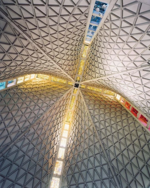 Interior shot of a domed building with a triangular pattern and cross-shaped windows, allowing light into the spacious architectural space.
