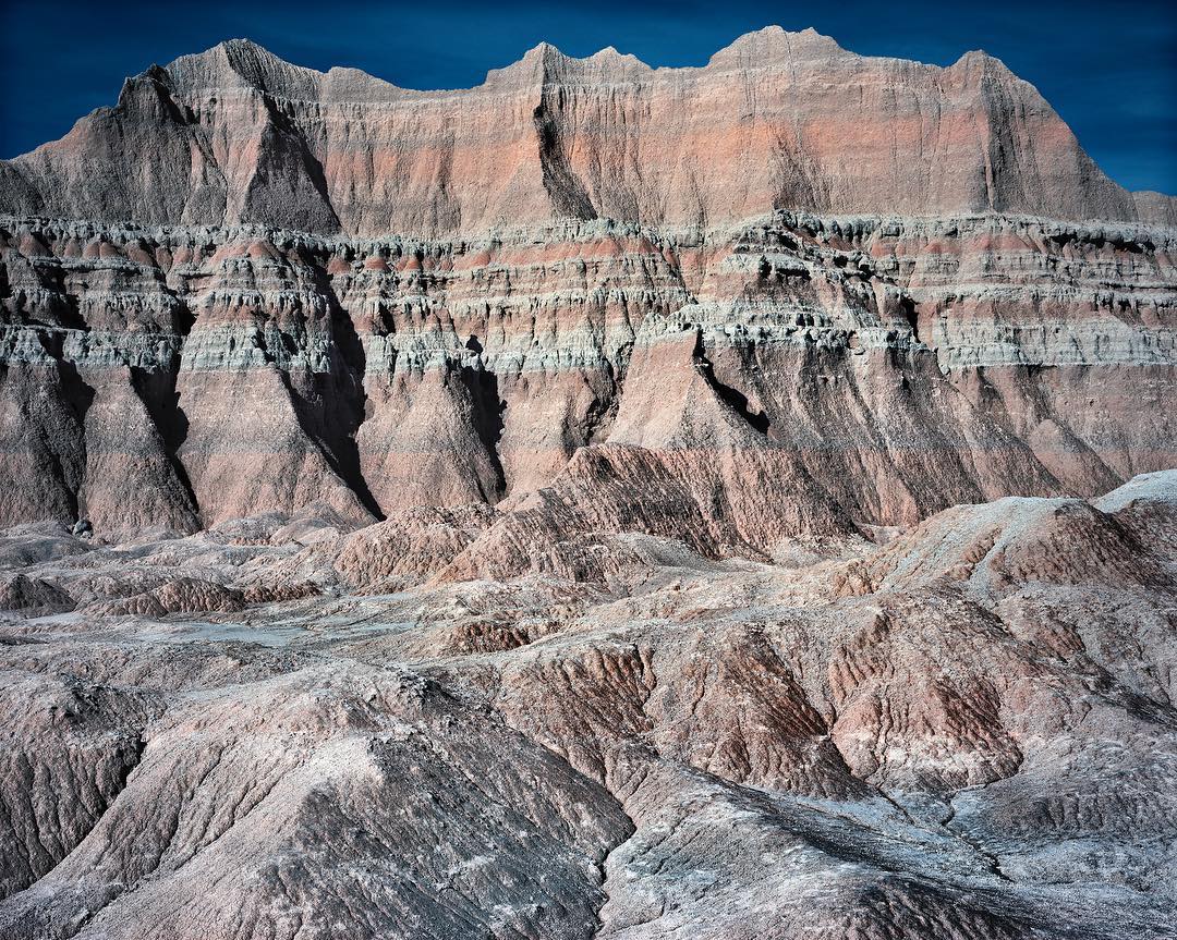 Panoramic view of a multi-layered mountain range with unique rock formations, showcasing textured surfaces and dramatic geological patterns under a clear sky.