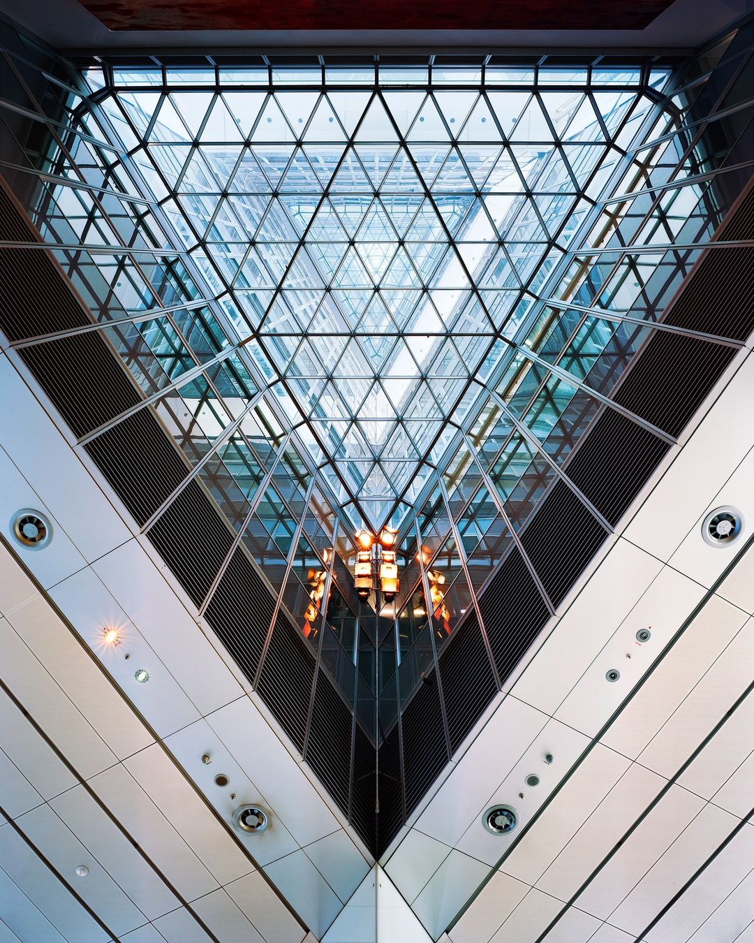 Interior view of a modern building with a triangular glass ceiling and intersecting architectural lines, creating a geometric pattern.