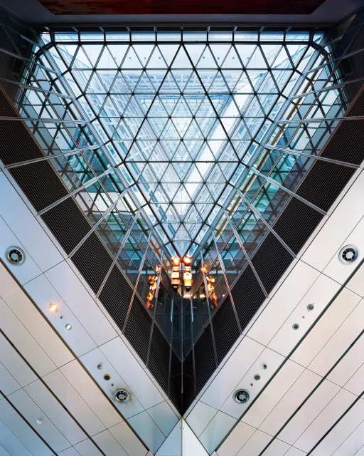 Interior view of a modern building with a triangular glass ceiling and intersecting architectural lines, creating a geometric pattern.