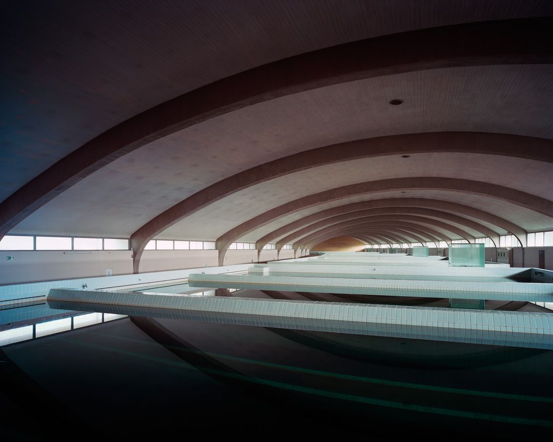 Indoor swimming pool interior featuring reflections in water and curved architecture in the ceiling, shot in wide angle.
