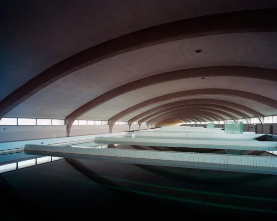 Indoor swimming pool interior featuring reflections in water and curved architecture in the ceiling, shot in wide angle.