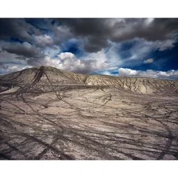 Arid landscape with tire tracks crisscrossing a dry hillside beneath a dramatic stormy sky with dark clouds