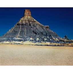 Factory Butte geological formation rising from flat arid desert landscape under a deep blue sky