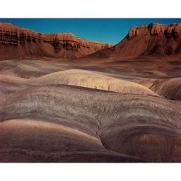 Arid desert landscape with rolling dunes and layered mountain ridges under a clear blue sky