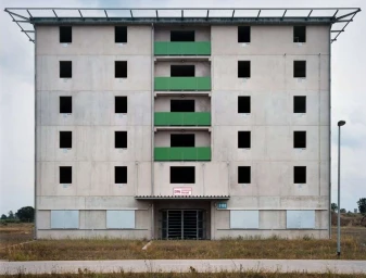 Symmetrical architectural photograph of a stark apartment building with green balconies and dark empty windows by Christoph Morlinghaus.