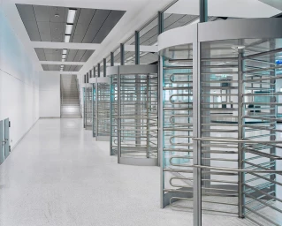 A row of glass and steel turnstiles in a modern white hallway photographed by Christoph Morlinghaus.