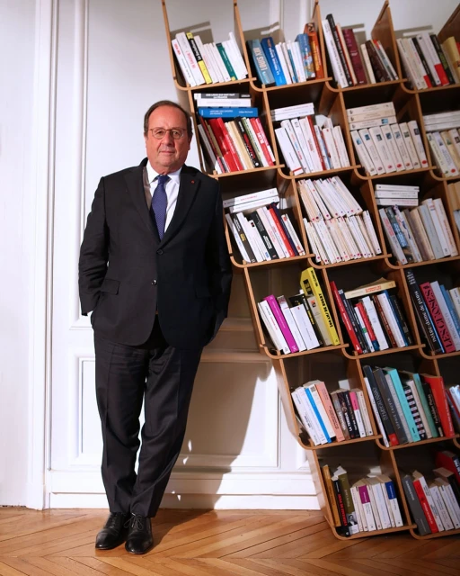 Portrait of a mature man in a suit leaning against a bookcase filled with books in an indoor setting, professional looking.