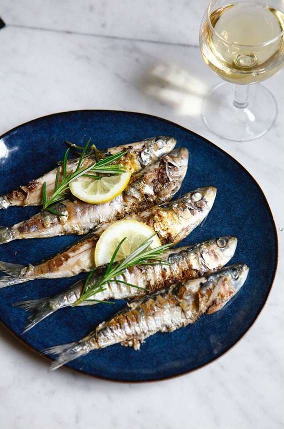 Overhead shot of a blue plate with grilled fish garnished with lemon and rosemary, accompanied by a glass of white wine.