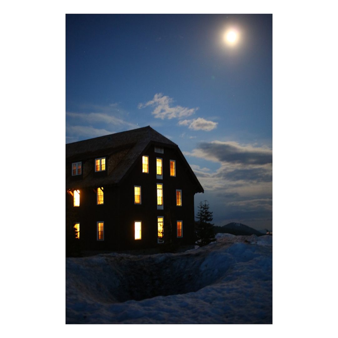 Exterior shot of a large building with illuminated windows against a twilight sky, with a snowy foreground and a bright moon.
