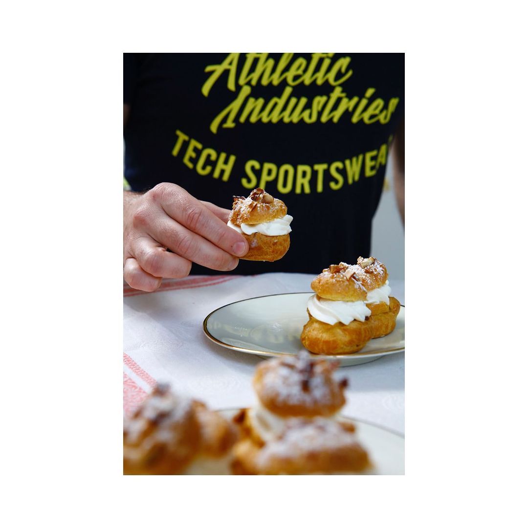 Cream puffs with powdered sugar are held and displayed on a plate with a black t-shirt in the background.