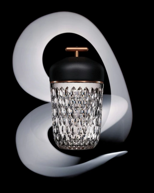 Crystal ice bucket with black leather lid and copper handle in a studio setting with white swirl and dark background.