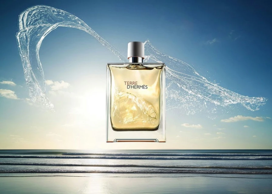 Terre d'Hermès fragrance bottle floats above a calm ocean during sunset, framed by water splashing and clear blue sky.