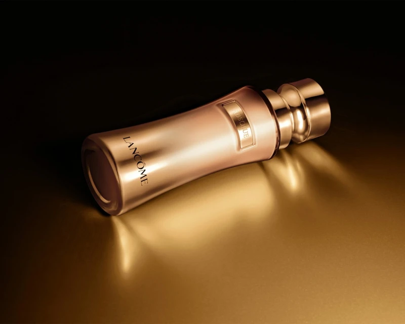 Elegant gold Lancôme Absolue skincare product bottle resting on a reflective gold surface in a photo studio setting with dark background.