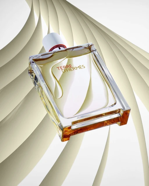 Angular view of Terre d'Hermès fragrance bottle against a white background with abstract paper-like shapes, showcasing a modern, minimalist aesthetic.