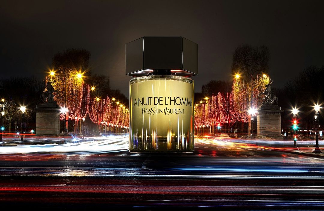 Yves Saint Laurent La Nuit de L'Homme fragrance bottle prominently displayed against a backdrop of blurred city lights at night.