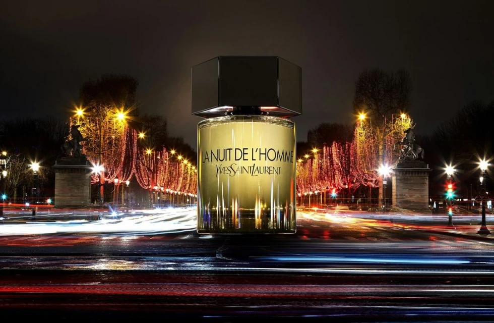 Yves Saint Laurent La Nuit de L'Homme fragrance bottle prominently displayed against a backdrop of blurred city lights at night.