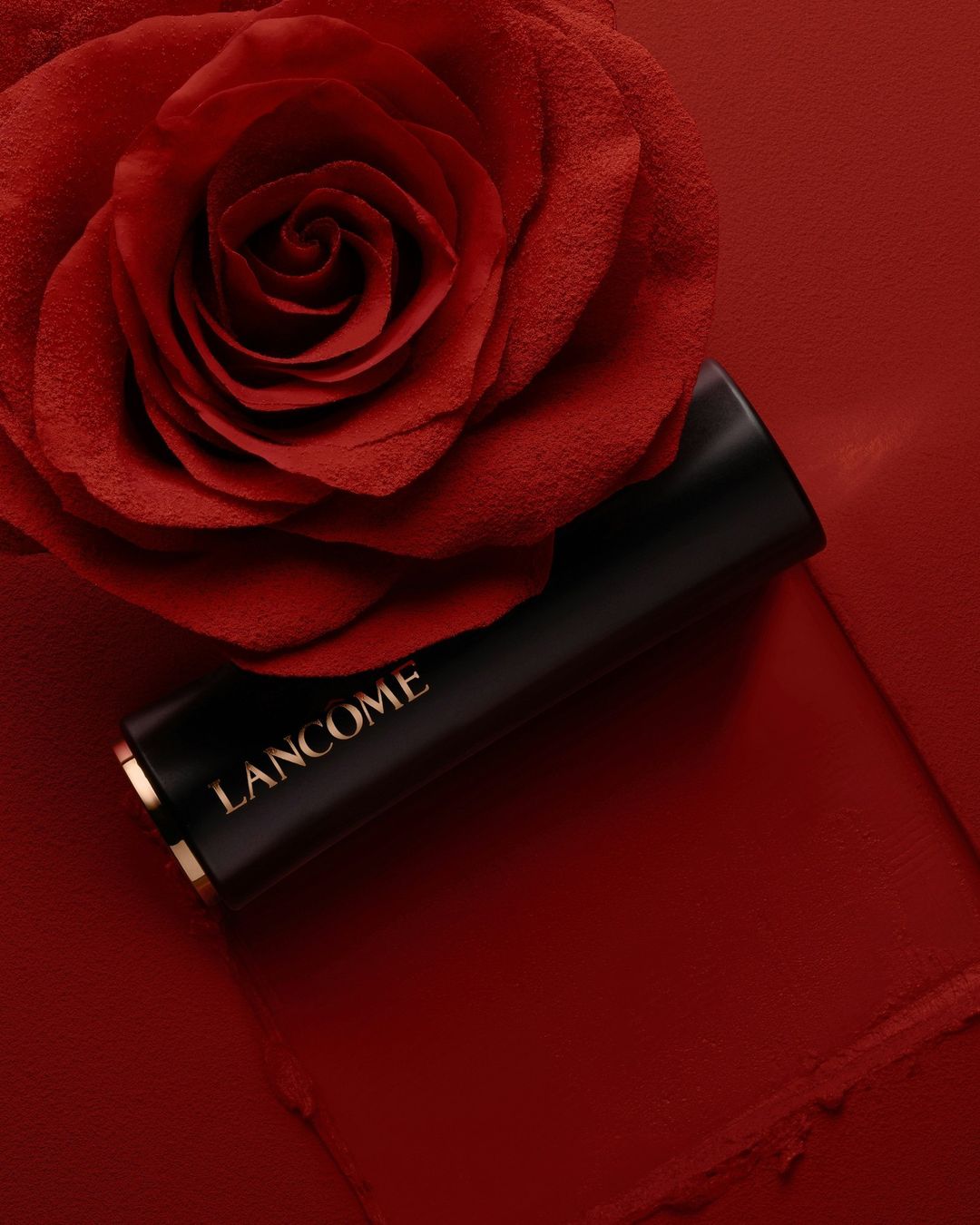 A close-up studio shot of a black Lancome lipstick tube on a red surface with a red rose, creating a luxurious and elegant beauty product image.