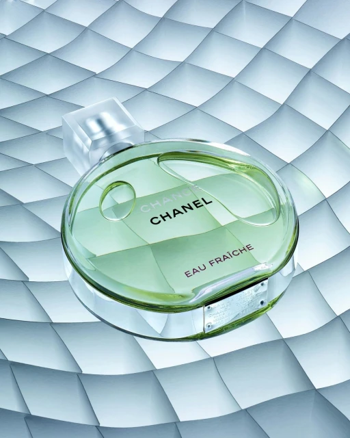 Green Chanel Chance Eau Fraiche perfume bottle on a textured, light blue background in a beauty still life product shot.