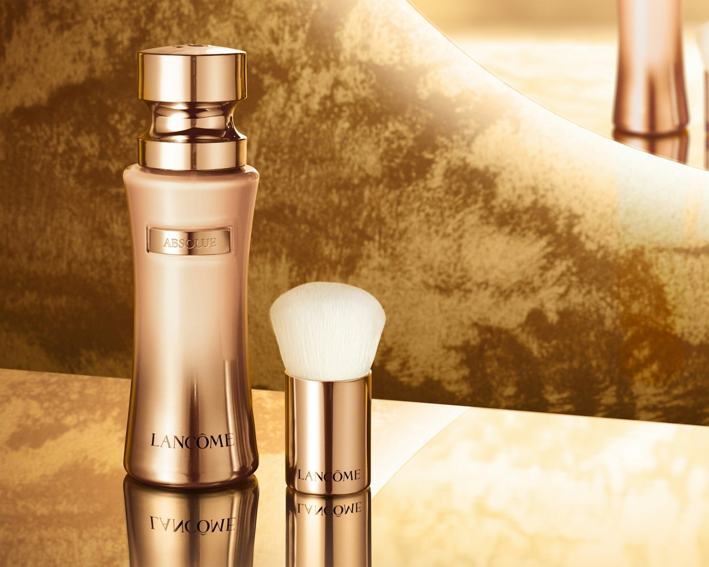 Elegant rose gold Lancôme Absolue beauty serum bottle and applicator brush, glossy reflective surface, and luxurious golden backdrop.