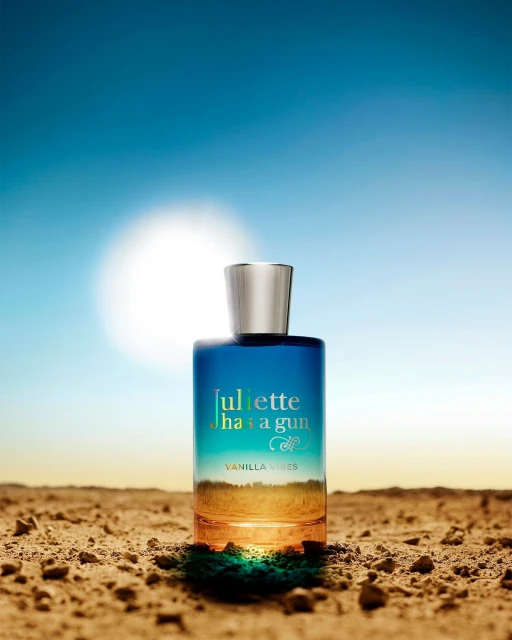 Blue and orange perfume bottle with a silver lid centered against a blue sky and desert landscape backdrop under natural lighting.