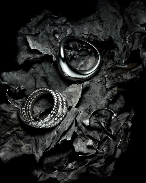 Silver rings and ear cuff jewelry arranged on crumpled sheet music paper with a dark, high-contrast fashion-style lighting scheme.