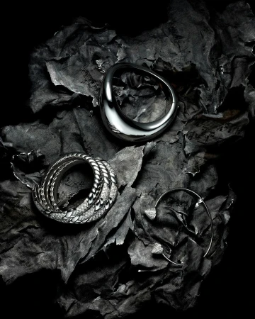 Silver rings and ear cuff jewelry arranged on crumpled sheet music paper with a dark, high-contrast fashion-style lighting scheme.