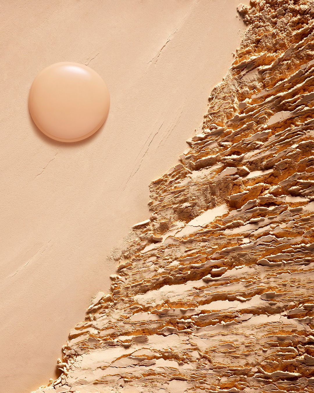Beige-toned beauty product shot featuring a round container next to a textured surface resembling compacted powder or ground material.