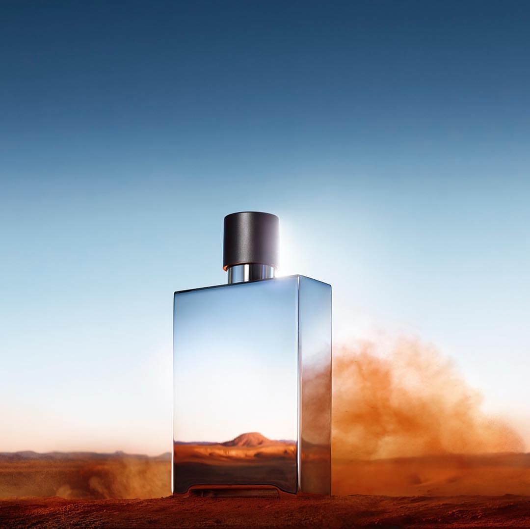 Rectangular perfume bottle reflecting a desert landscape with orange soil and a blue sky background, showcasing product photography.