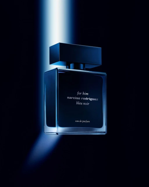 Studio shot of a "for him" Narciso Rodriguez Bleu Noir eau de parfum bottle in a dark blue hue, illuminated by a bright light.