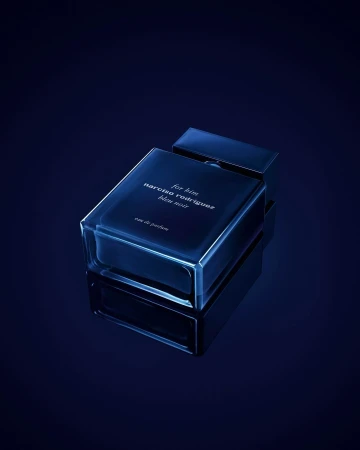A rectangular dark blue perfume bottle resting on a dark reflective surface under moody blue lighting.