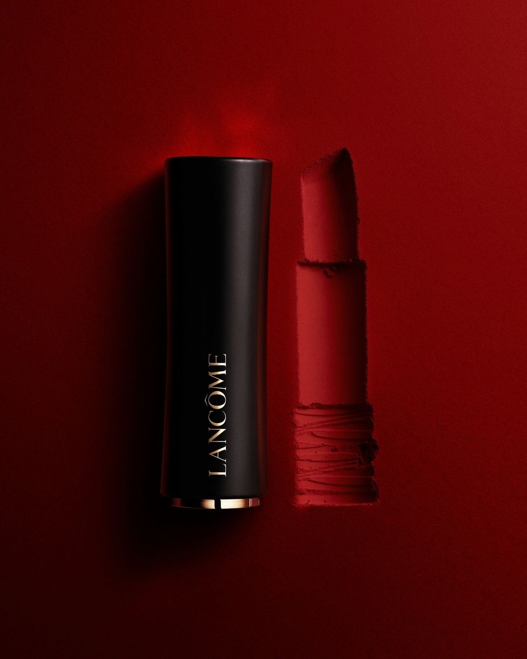 Lancôme lipstick tube in black and gold next to open red lipstick on red background for beauty and fashion advertising.