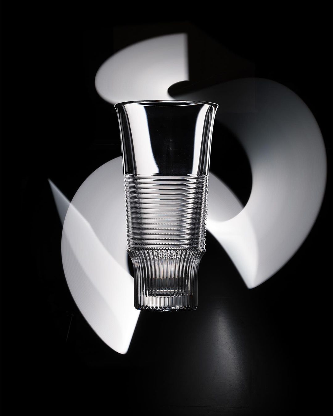 Elegant crystal glass with ribbed details on a dark backdrop with blurred white light streaks creating a dynamic, eye-catching visual effect.