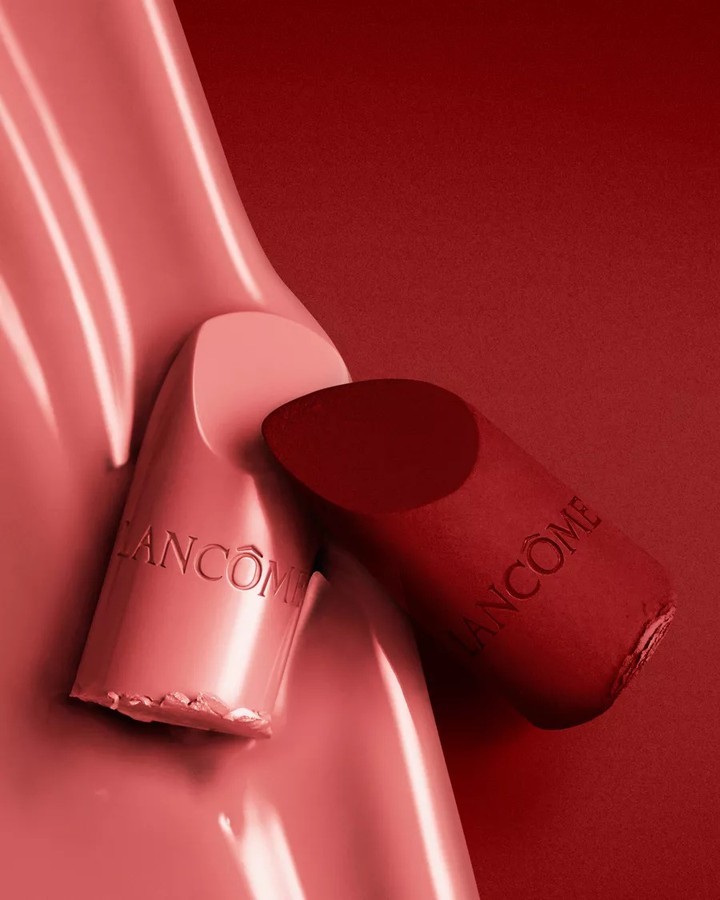 Two pieces of Lancôme lipstick in light pink and deep red are set against a red backdrop in a beauty product shot.
