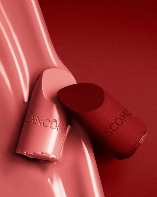 Two pieces of Lancôme lipstick in light pink and deep red are set against a red backdrop in a beauty product shot.
