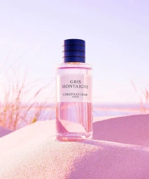Christian Dior Gris Montaigne perfume bottle standing upright in sandy dunes under soft pink sunlight.
