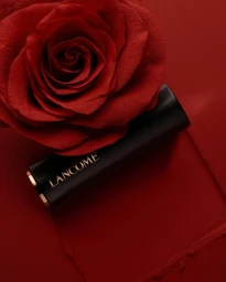 Lancome lipstick tube resting next to a large red rose against a matching textured red surface