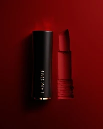 Lancome lipstick with black case and red bullet positioned upright against a deep red textured background.