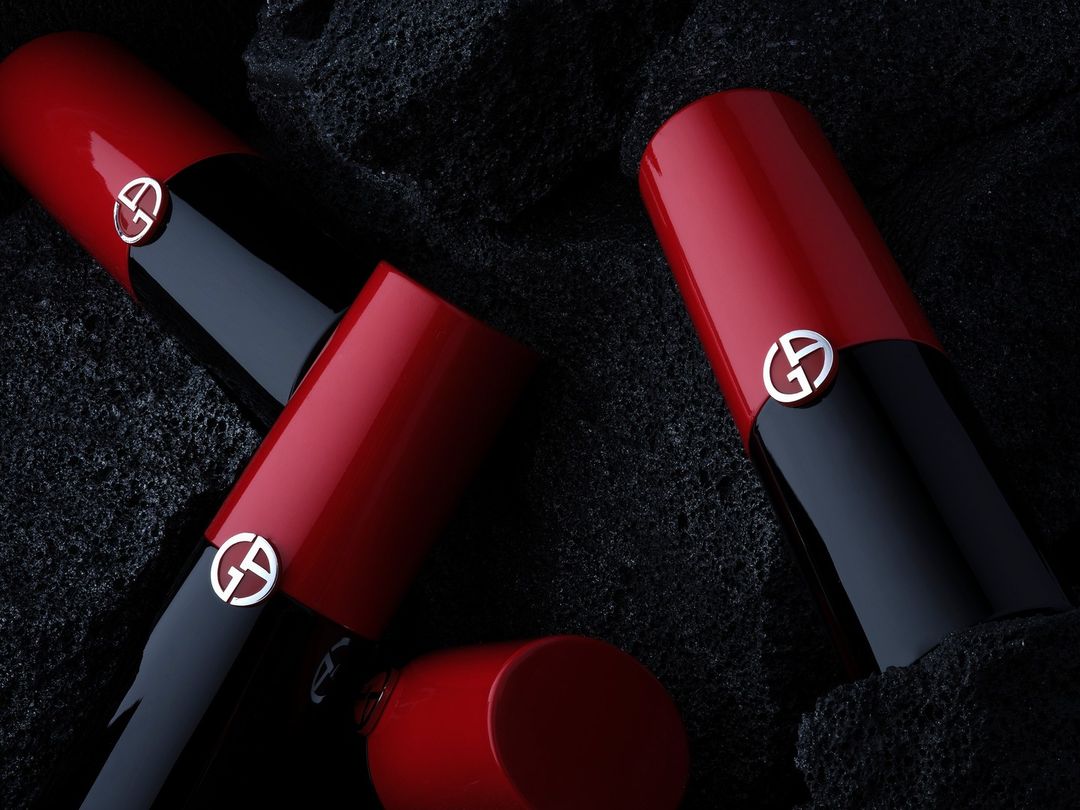 Close-up studio shot of three Giorgio Armani lipsticks, featuring red and black tubes with the brand's iconic 'GA' logo. Beauty shot.