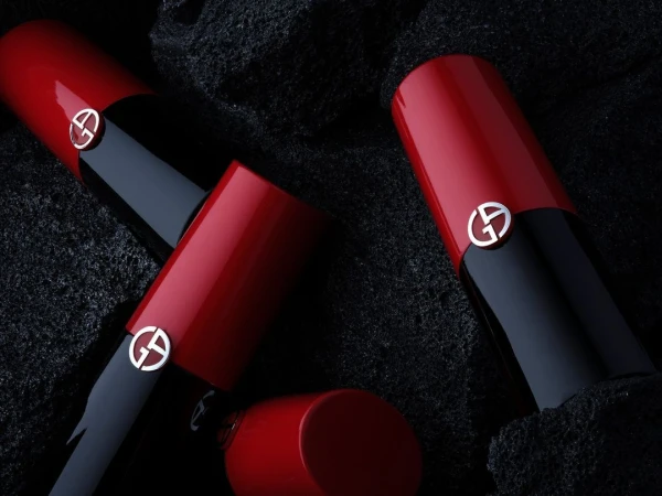 Close-up studio shot of three Giorgio Armani lipsticks, featuring red and black tubes with the brand's iconic 'GA' logo. Beauty shot.
