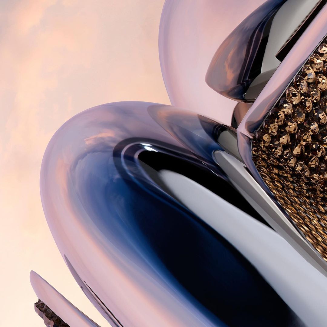Abstract chrome sculpture with amber honeycomb pattern against a light pink sky background with clouds reflecting on the metal surface.