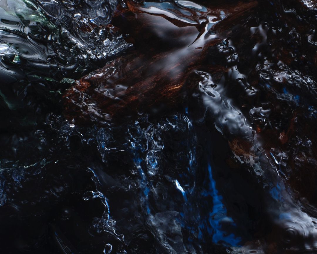 Abstract macro photograph of turbulent, dark water with hints of blue, brown, and white, creating a dynamic and fluid texture.