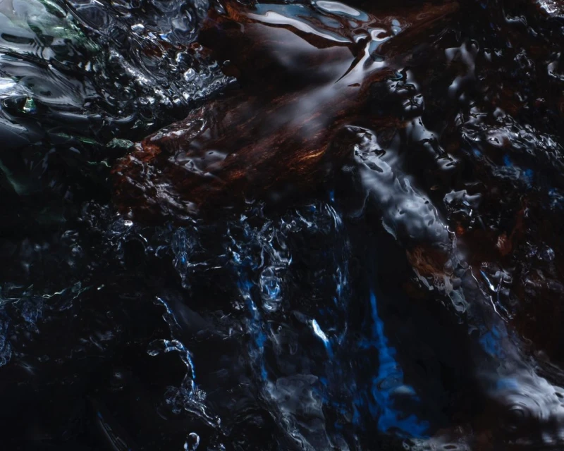 Abstract macro photograph of turbulent, dark water with hints of blue, brown, and white, creating a dynamic and fluid texture.