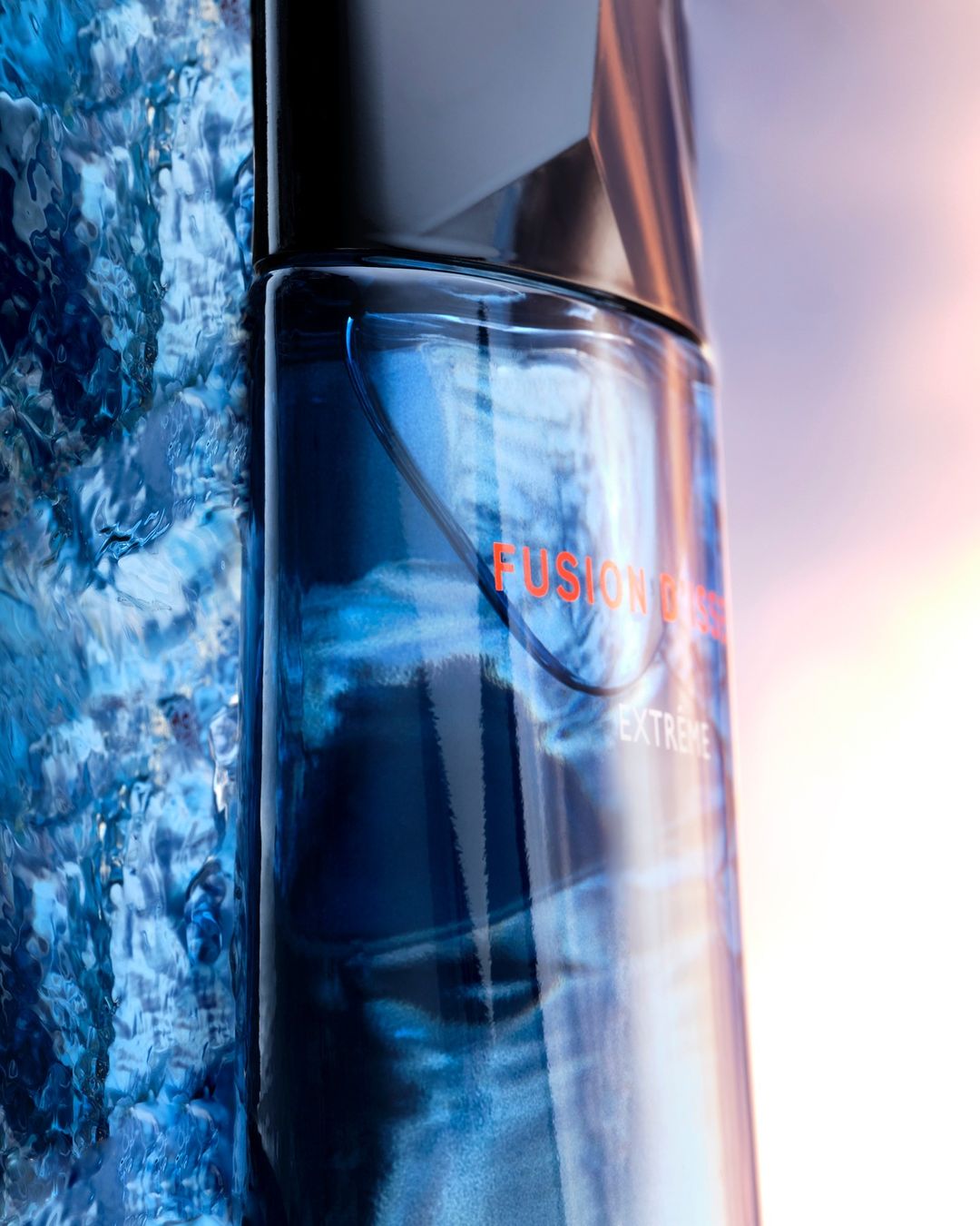 Close-up of a blue glass cologne bottle with orange text on a textured blue and white background with subtle light reflections.