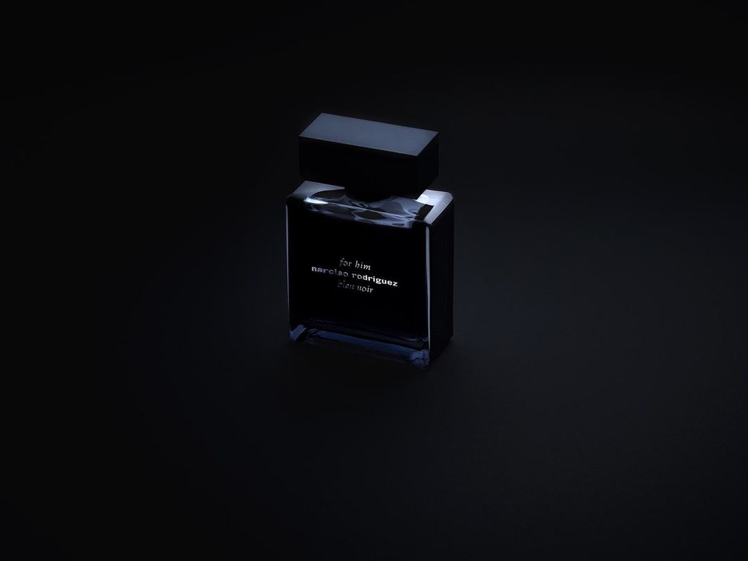 Dark rectangular perfume bottle with a black cap resting on a dark surface under low-key lighting