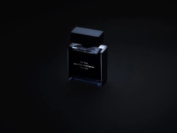 Dark rectangular perfume bottle with a black cap resting on a dark surface under low-key lighting