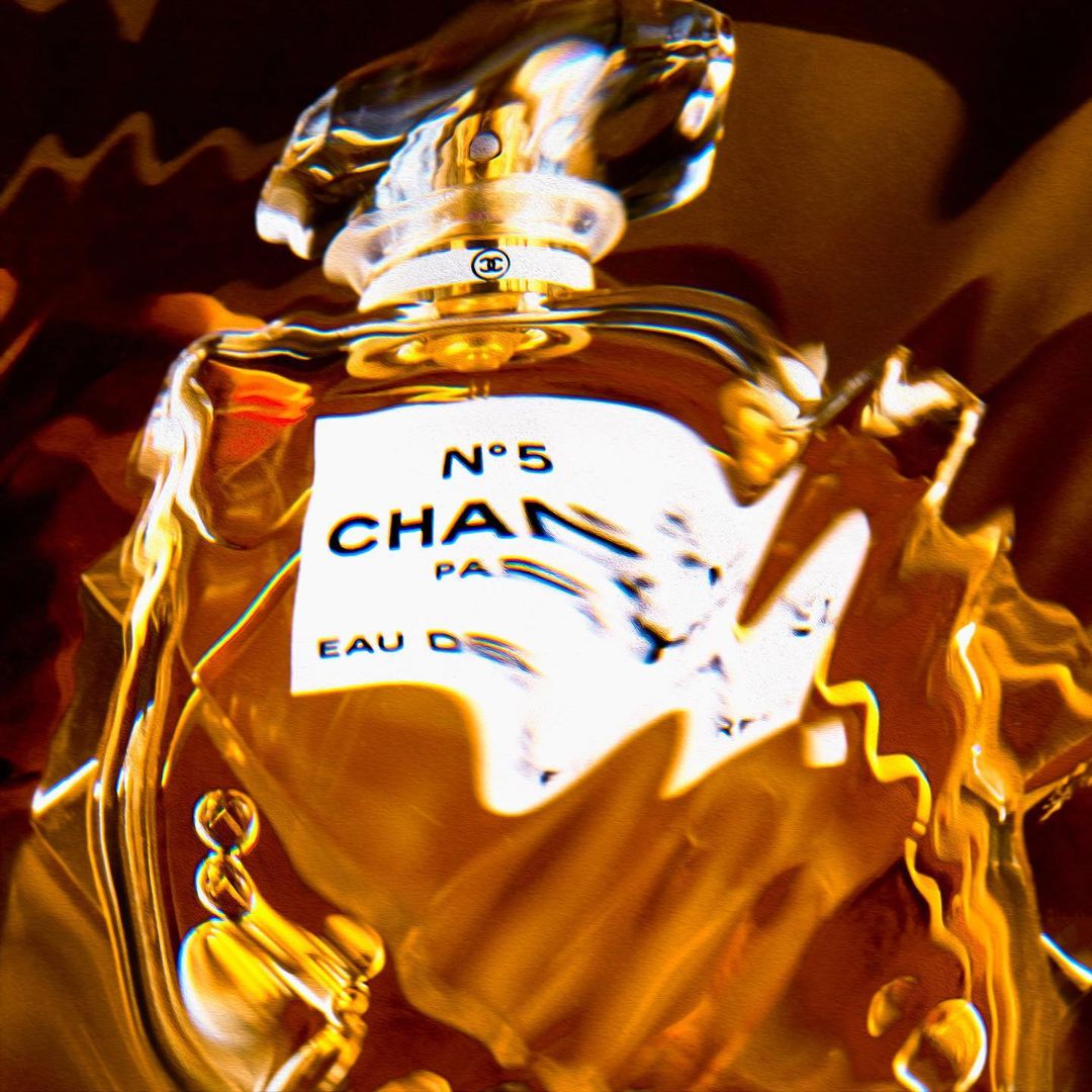 Close-up of a Chanel N°5 perfume bottle, featuring a clear glass bottle and stopper, gold liquid, and distinct product label. Studio lit.